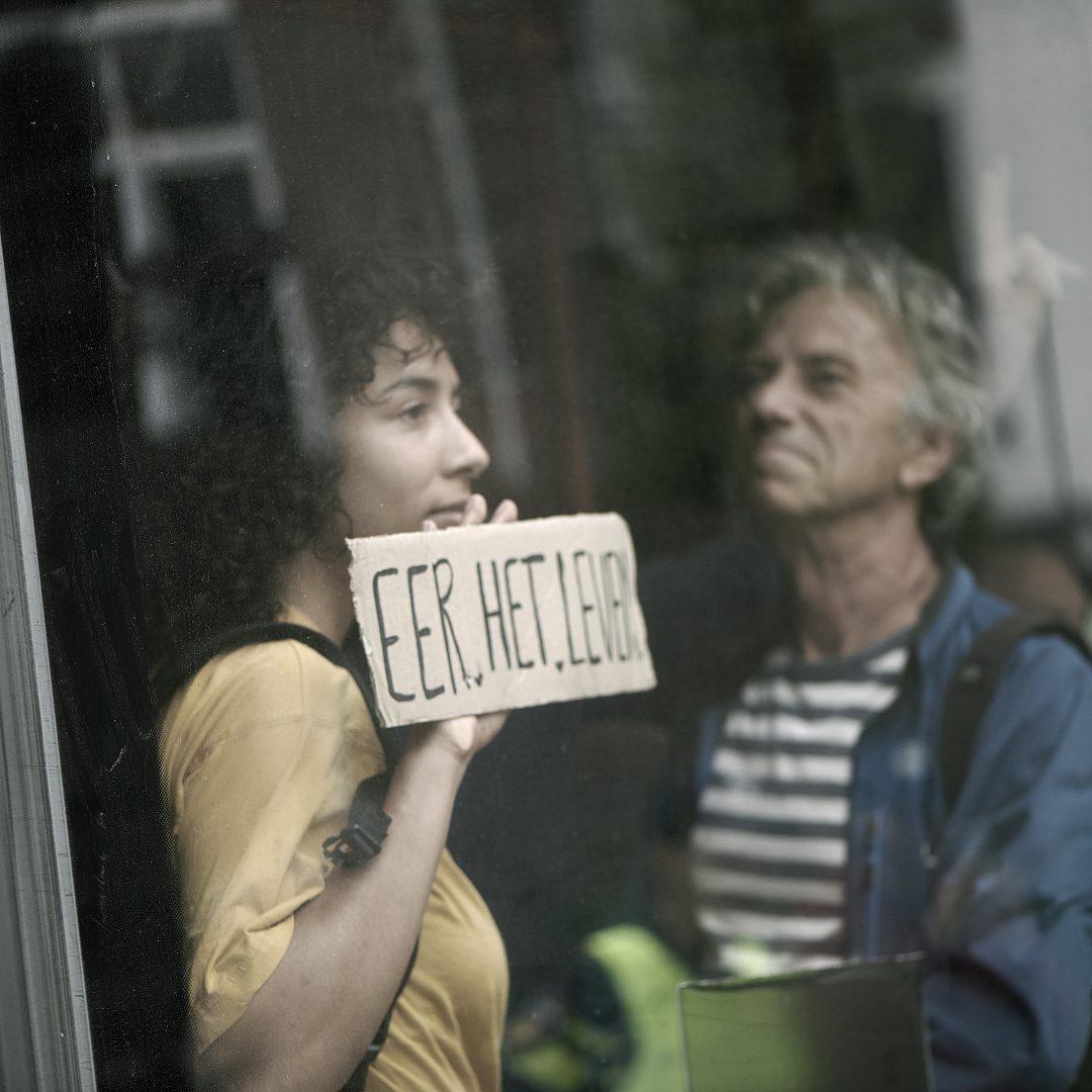 Jonge demonstrant houdt bord ‘Eer het leven’ tegen busraam tijdens klimaatprotest Extinction Rebellion Den Haag