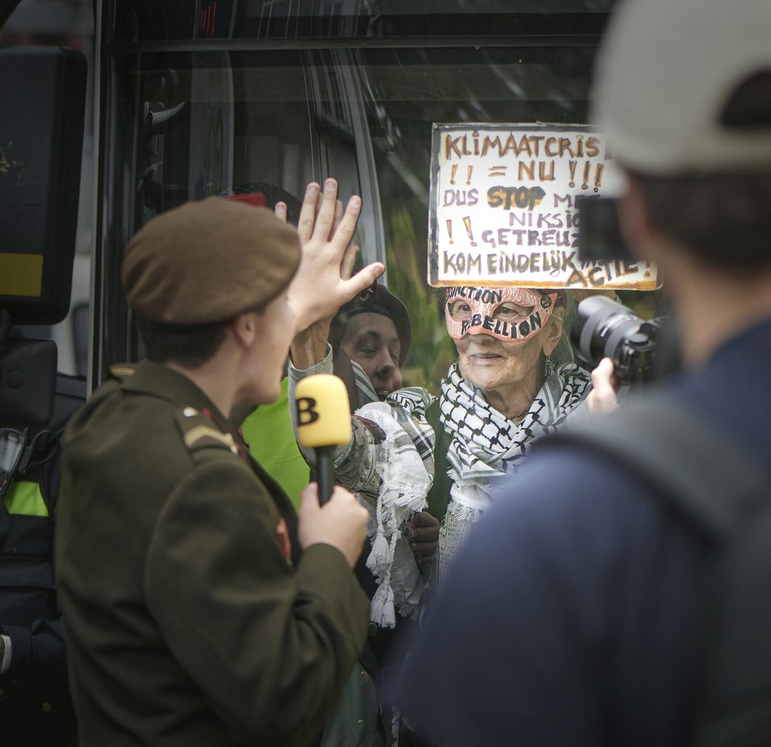 Verslaggever legt hand tegen raam van bus als gebaar naar klimaatactivist tijdens demonstratie in Den Haag
