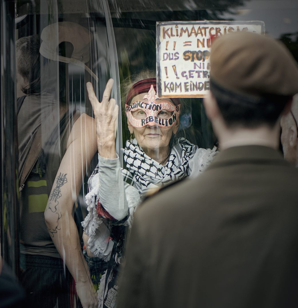 Oudere demonstrant in bus houdt bord omhoog over klimaatcrisis tijdens protest Den Haag 2025